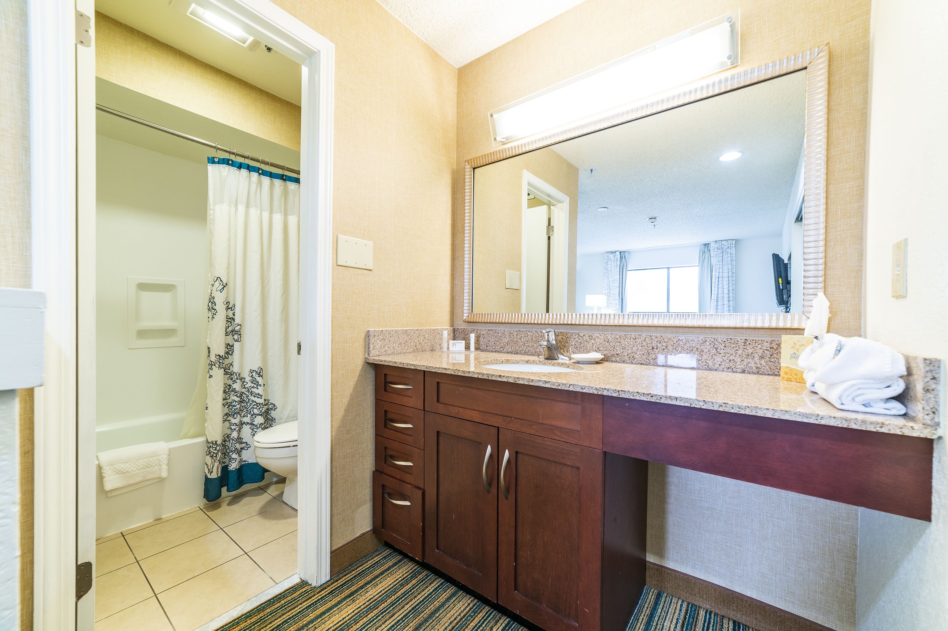 A bathroom with a shower, toilet, sink, and a large mirror.
