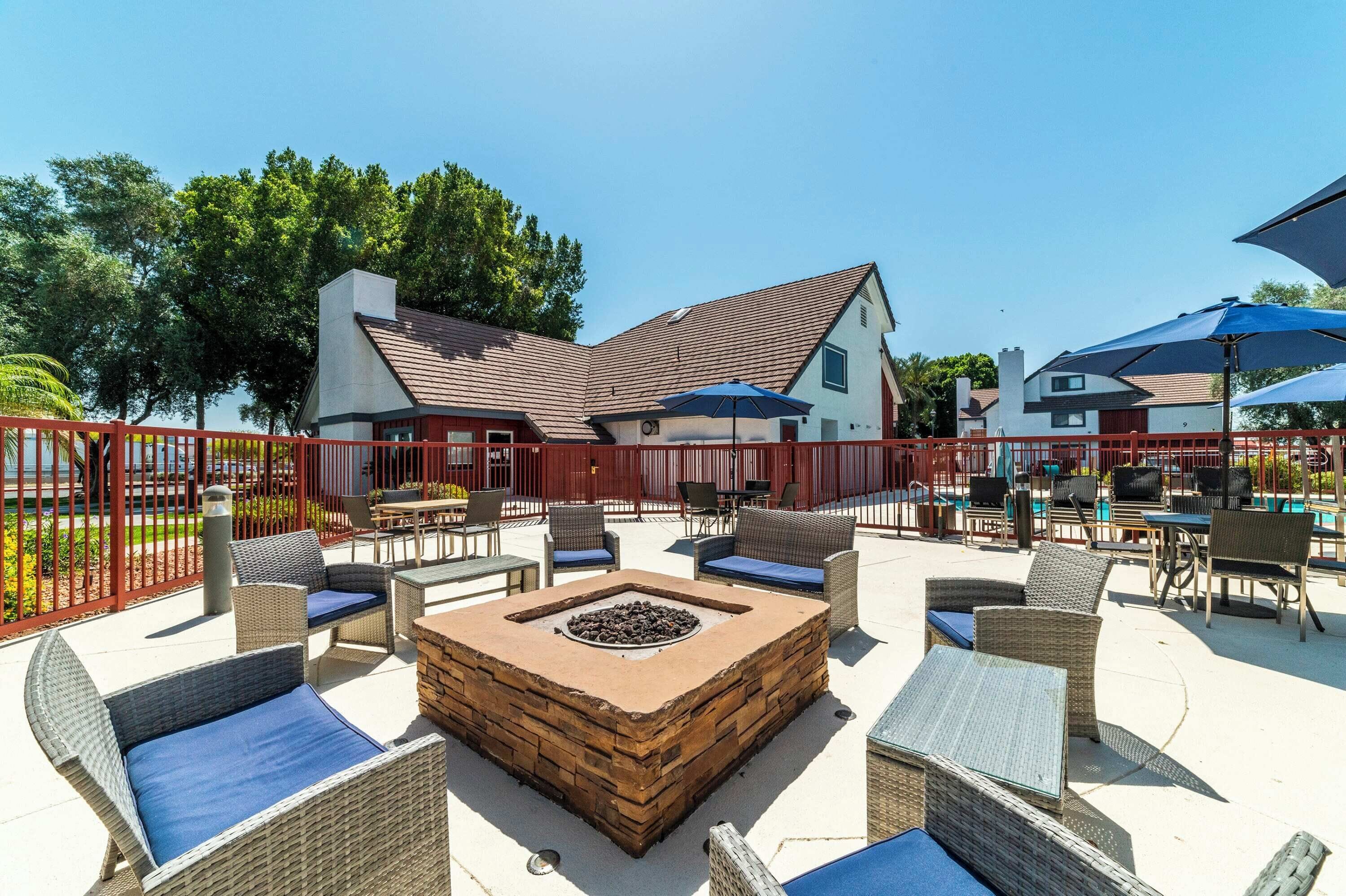 An outdoor patio with wicker furniture, a fire pit, and umbrellas.