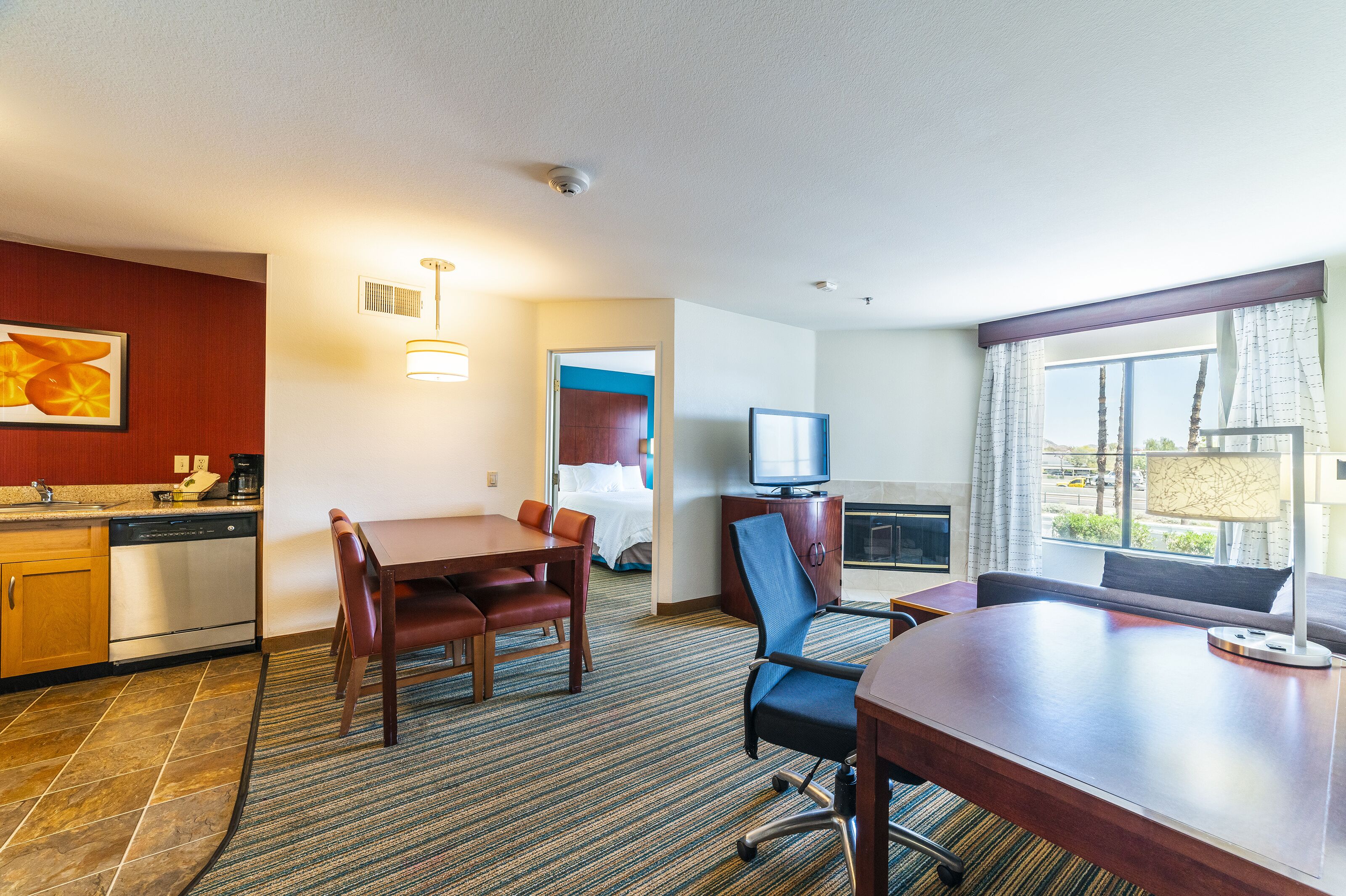 Habitación de hotel con comedor, televisor, chimenea y un amplio ventanal con vistas.