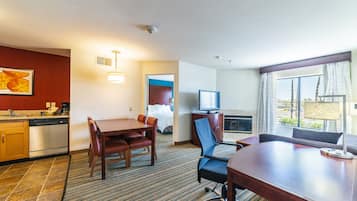 A hotel room with a dining area, a television, a fireplace, and a large window with a view.