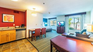 A hotel room with a kitchenette, a dining area, a sofa, a TV, and a window with a view. - Metro Phoenix Extended Stay (Phoenix)