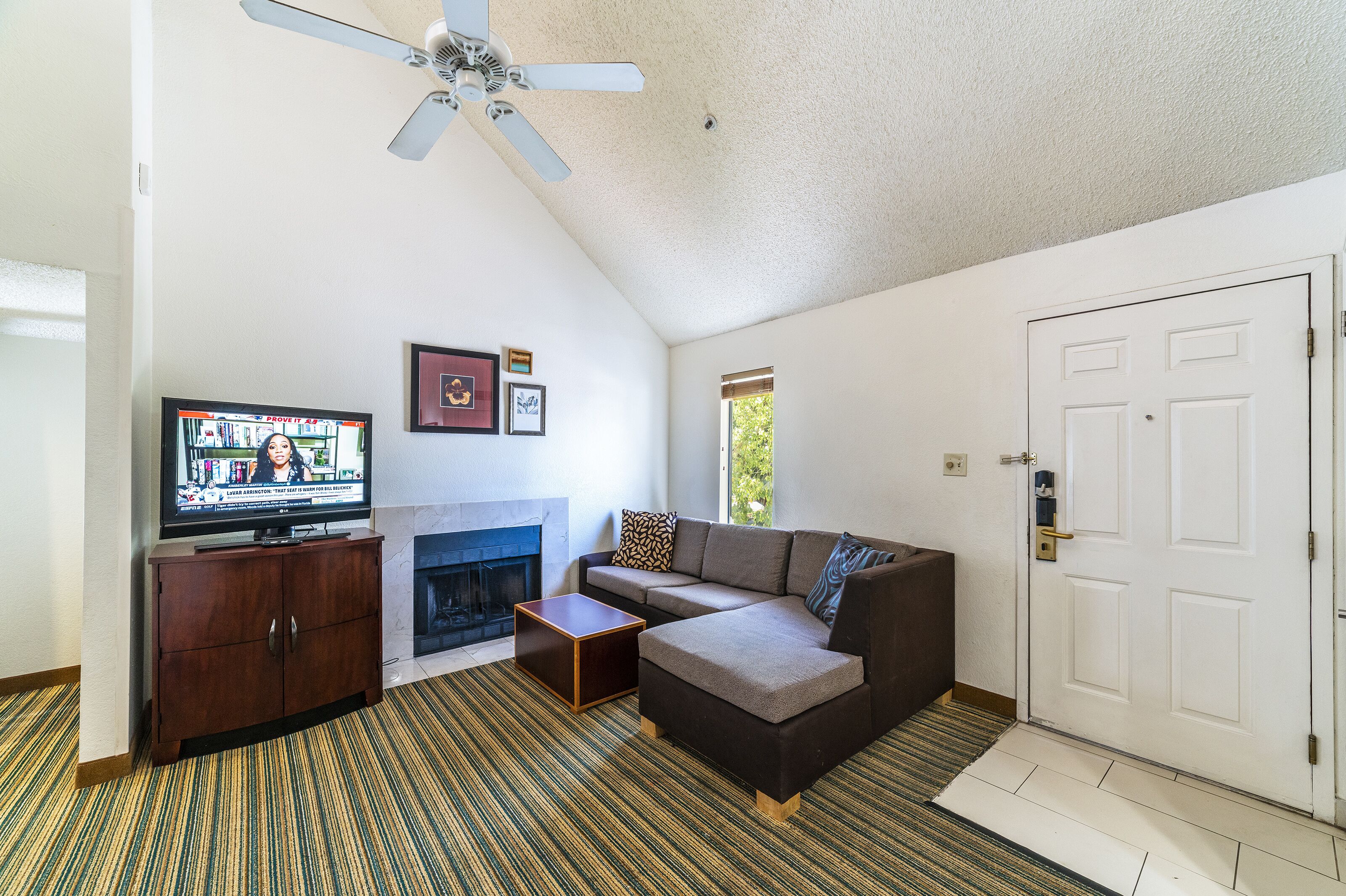 A living room with a sofa, a television, a fireplace, and a ceiling fan.