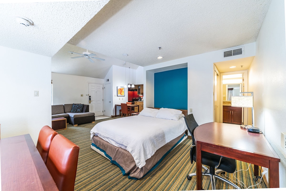 Quarto de hotel com cama, escrivaninha, cadeira, sofá e mesa de jantar.