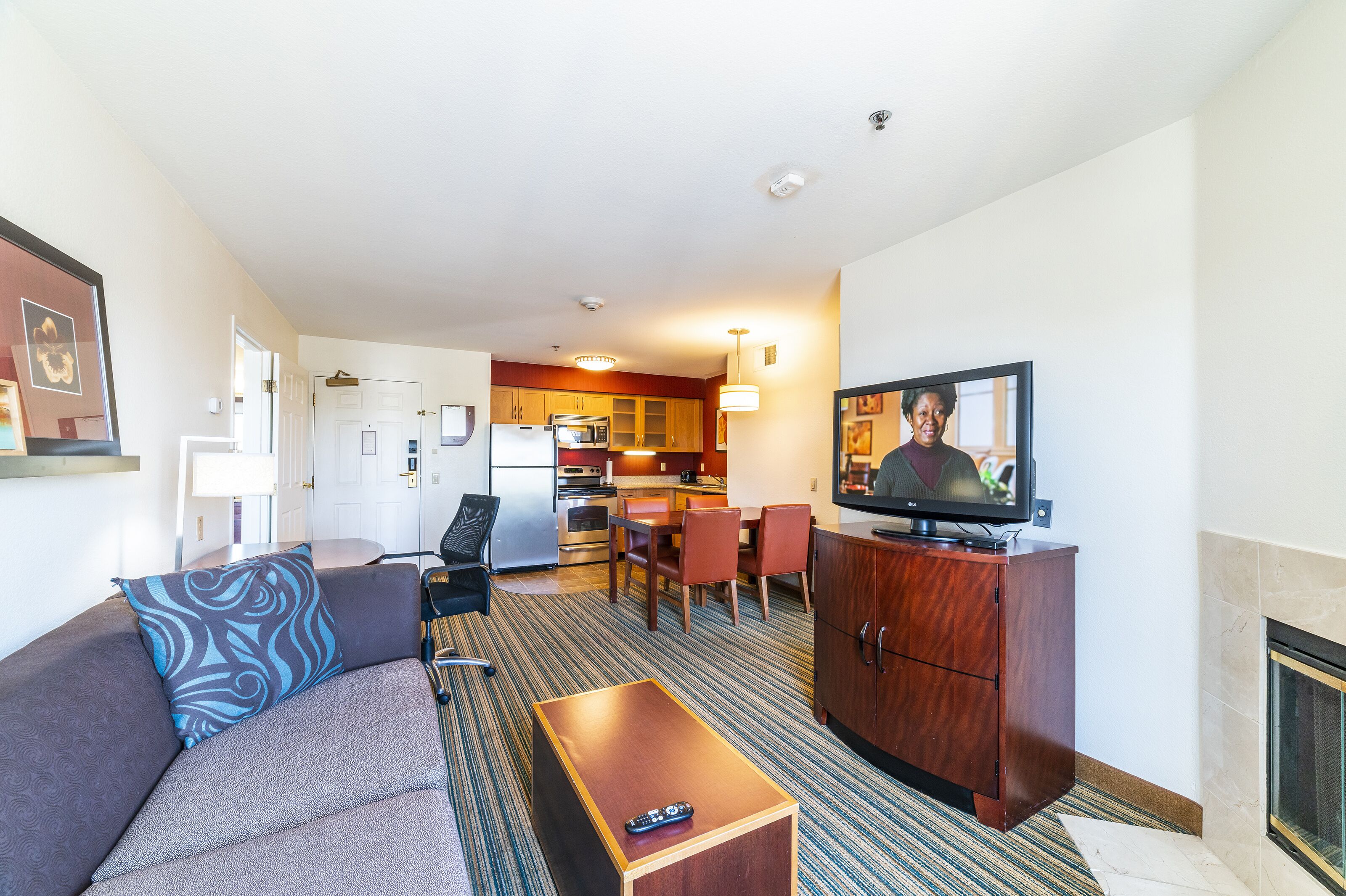 Une chambre d’hôtel compacte comprenant un canapé, une table basse en bois, une télévision, une kitchenette et une cheminée.