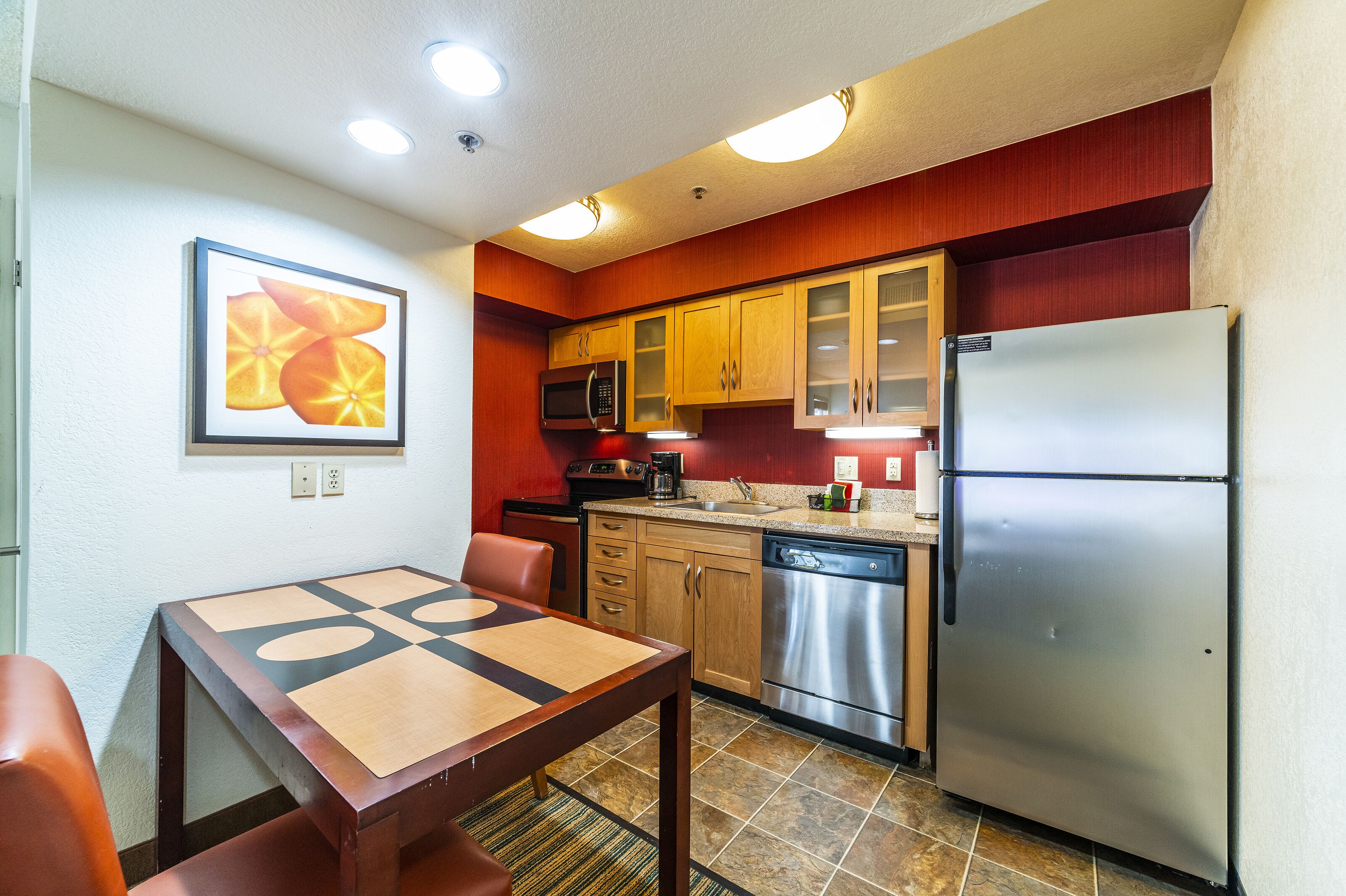 A compact kitchen with wooden cabinets, a stainless steel refrigerator, a microwave, and a dishwasher.