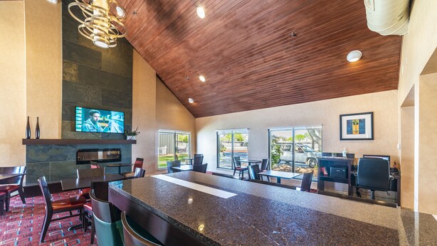A modern bar area with a granite countertop, seating, a television, and a stone fireplace. - Metro Phoenix Extended Stay (Phoenix)