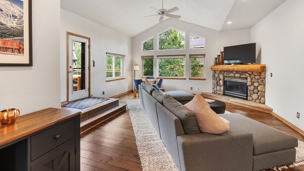 A spacious living room with a stone fireplace, a large gray sofa, and a ceiling fan. - Luxury Home-Walk to everything in Frisco. Hot tub, ski, fireplace 3BD, 3.5BA



 (Frisco)