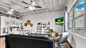 Ein modernes Wohnzimmer mit einer schwarzen Couch, einem grauen Sessel und einem Fernseher an der Wand.