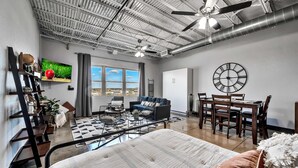 Ein modernes Wohnzimmer mit Sofa, Esstisch, Stühlen, großen Fenstern und Deckenventilator.