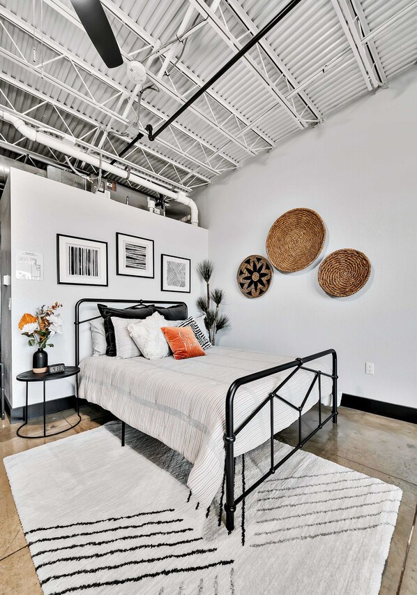 A modern bedroom with a metal bed frame, a white bedspread, and decorative woven wall art. - Silo Boho Bungalow - Downtown Waco (Waco)