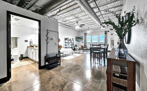 A spacious living area with a high ceiling, a dining area, and a kitchen visible through an open doorway. - Silo Boho Bungalow - Downtown Waco (Waco)