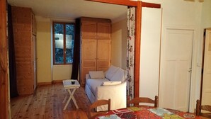 Una habitación acogedora con piso de madera, una cama con cabecera blanca, una mesita con una taza, y un colcha colorida sobre el piso.