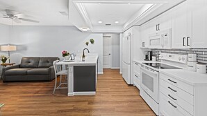 Una cocina moderna con armarios blancos, una isla central y un rincón comedor con sofá y sillas.