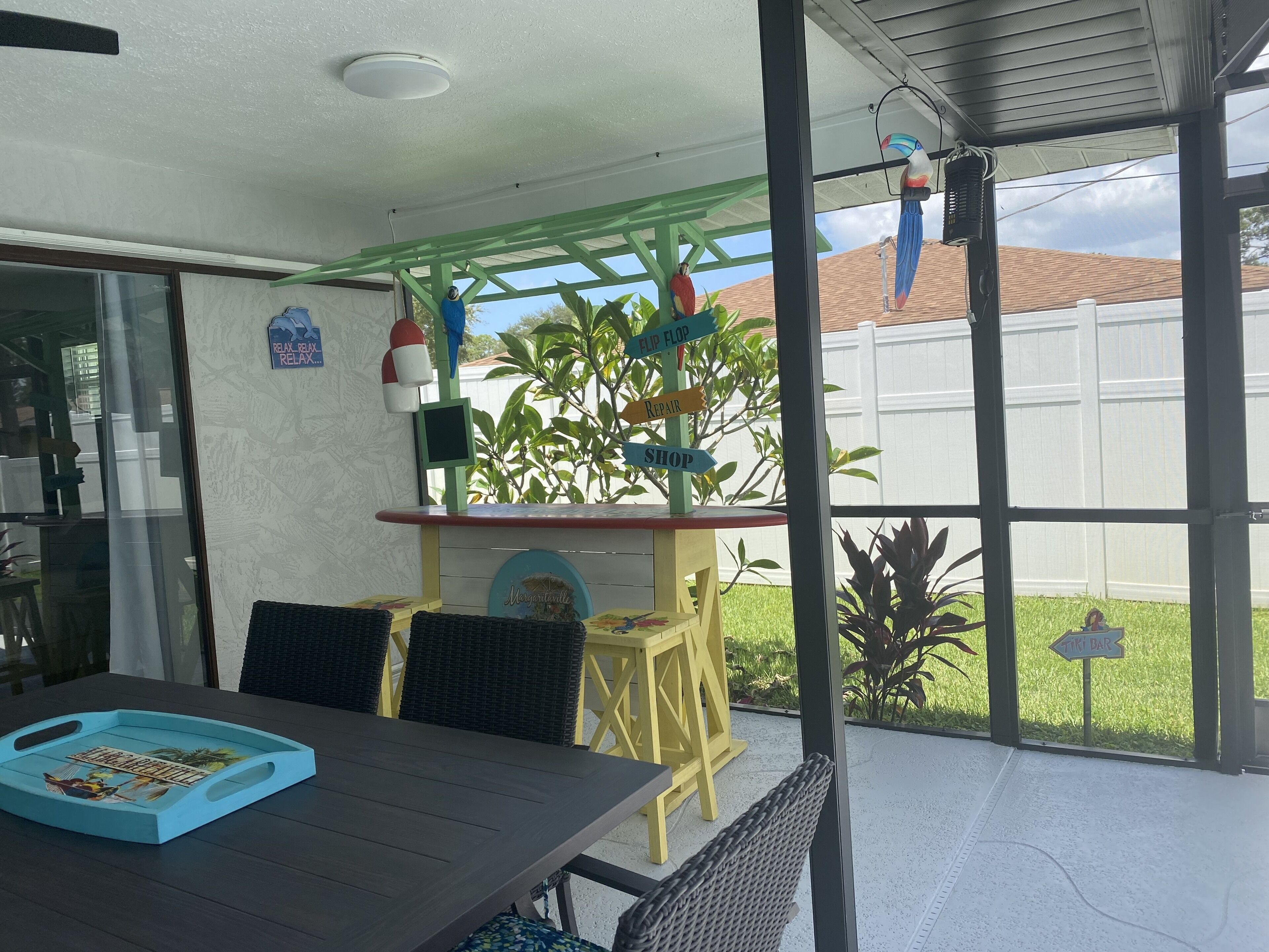 A patio area with a table and chairs, a small bar area, and a view of a white fence and greenery.