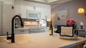 Una cocina moderna con armarios blancos, un microondas y una botella de vino en la encimera.