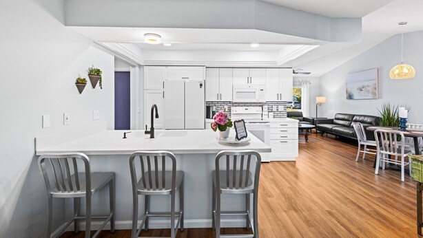 Una cocina moderna con armarios blancos, una isla central con taburetes y un comedor con mesa y sillas.
