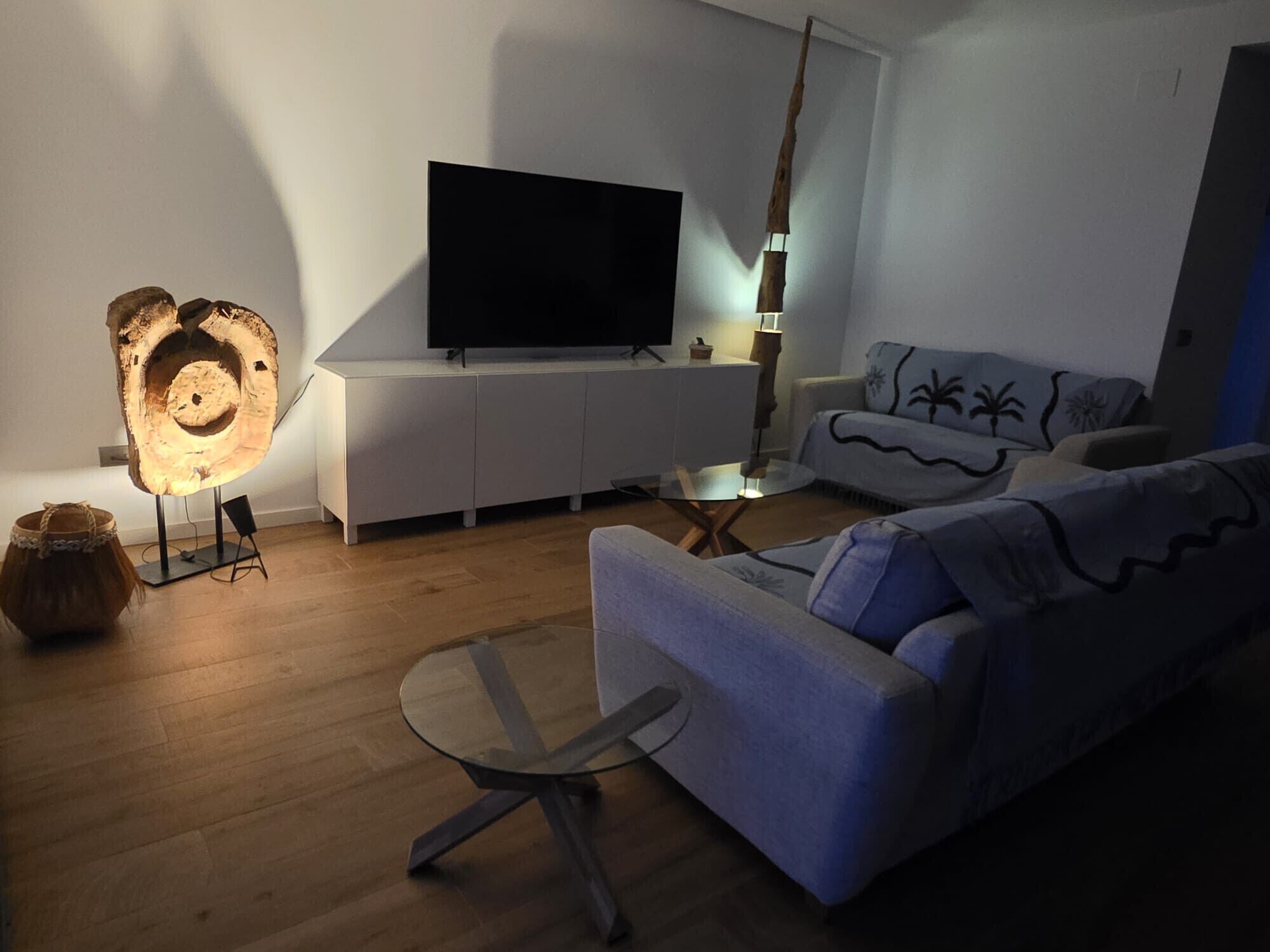 A modern living room with a flat-screen TV, a unique wooden sculpture, a sofa, and a glass coffee table.