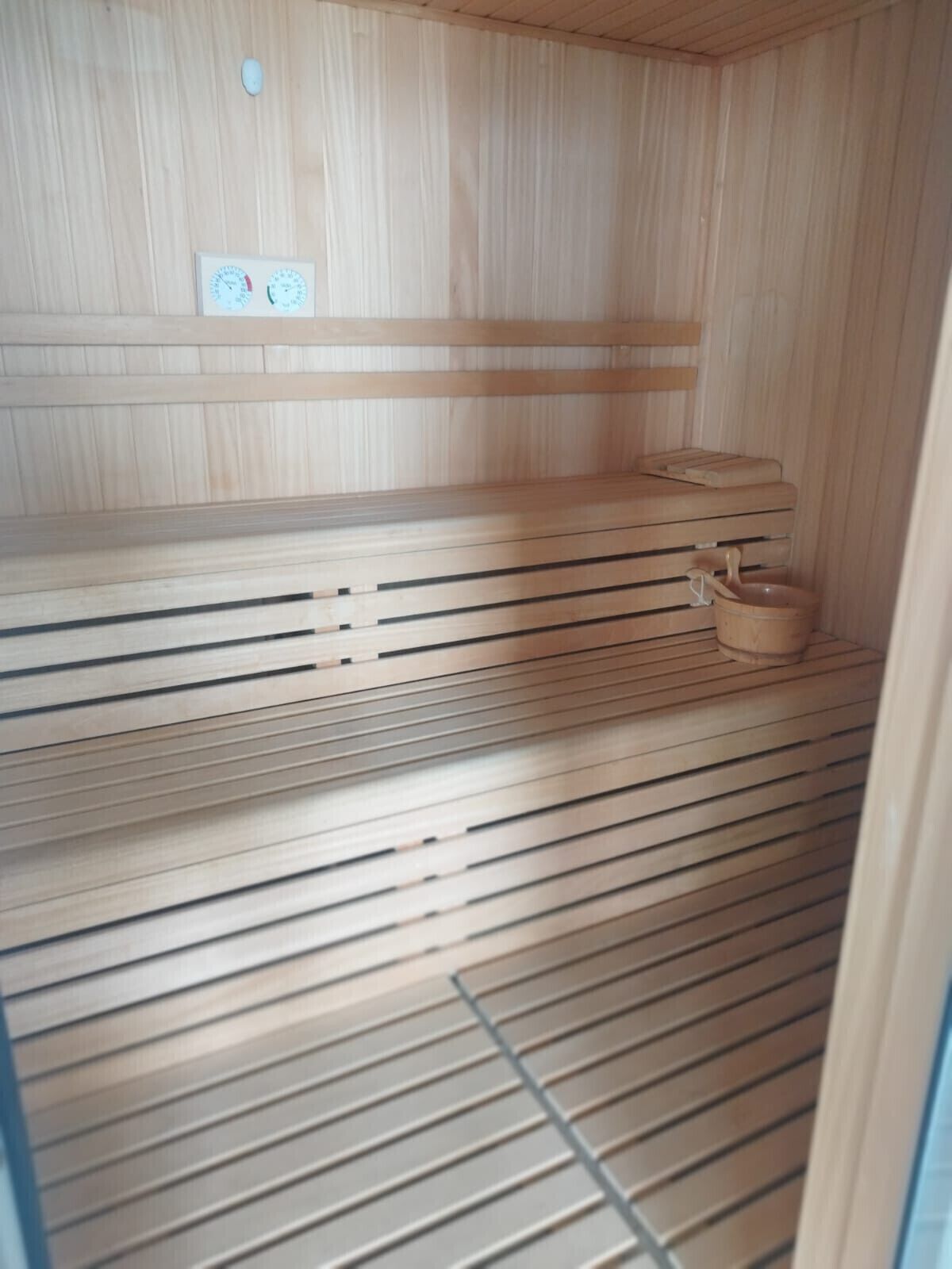 Una sauna con bancos de madera y un balde pequeño de madera.