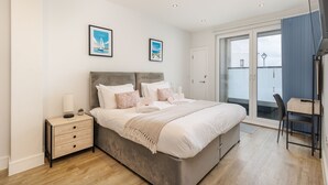 Un dormitorio con cama, mesitas de noche, escritorio y balcón.