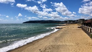 Una playa con un paseo de madera, un muelle y edificios al fondo.