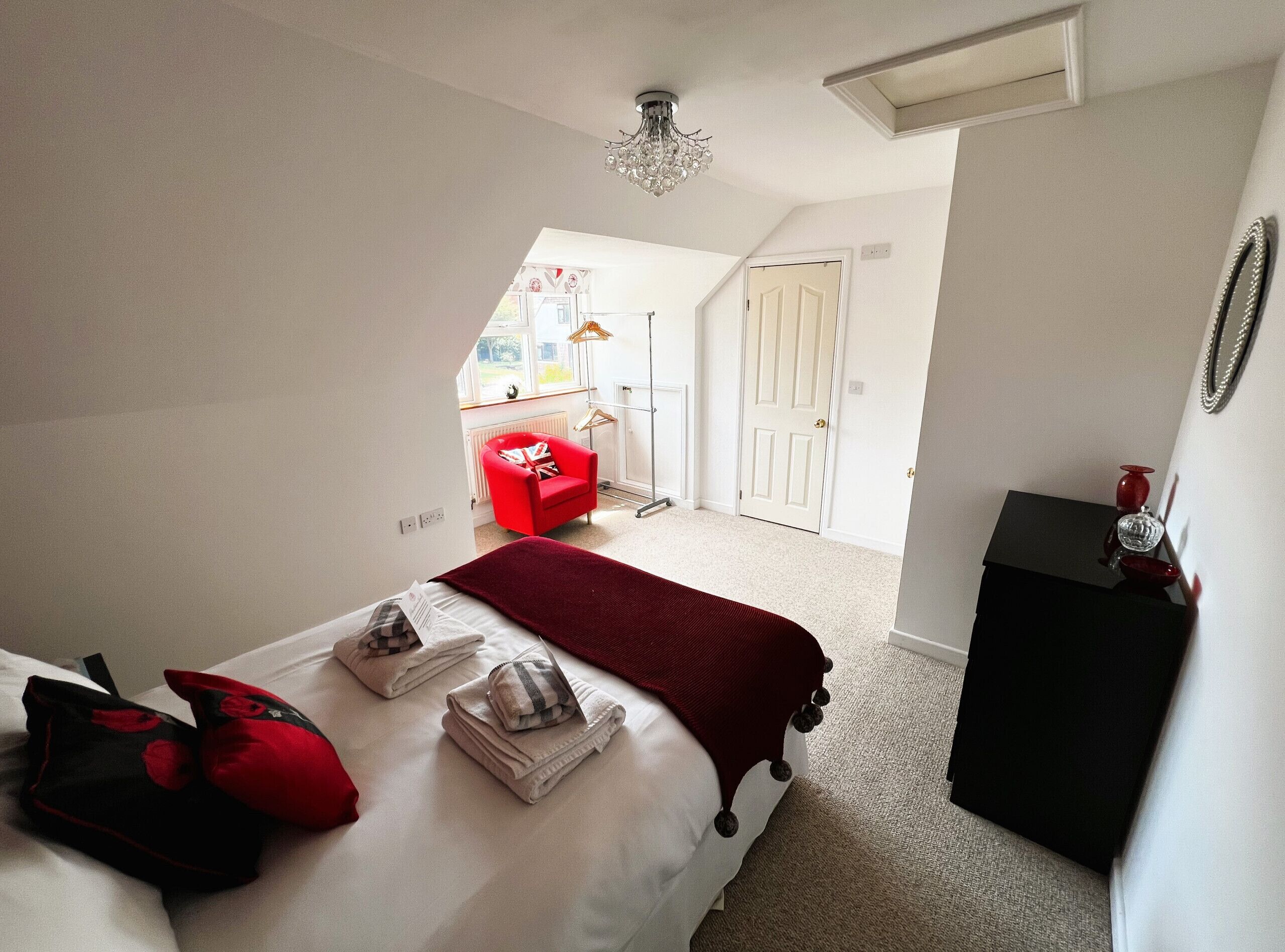 Un dormitorio con una cama bien hecha, un sillón rojo y un aparador negro.