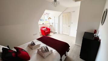 Un dormitorio con una cama bien hecha, un sillón rojo y un aparador negro.