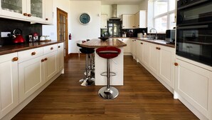 A kitchen with white cabinets, a wooden countertop, a red kettle, and a clock on the wall. - Littlestairs (Shanklin)