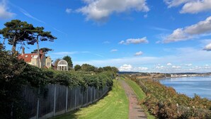 A coastal pathway with a wooden fence and a grassy area leading to a body of water. - Littlestairs (Shanklin)