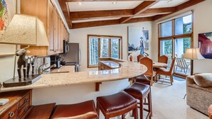 A kitchen with a curved island, wooden cabinets, and a dining area with chairs and a table. - Ski-in Condo w Vail Views near Gondola, TT5C (Vail)