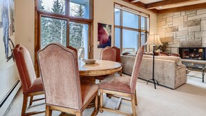 A cozy living room with a stone fireplace, large windows, and a round dining table with chairs. - Ski-in Condo w Vail Views near Gondola, TT5C (Vail)
