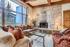 Un salon chaleureux avec une cheminée en pierre, de grandes fenêtres et des sièges confortables.