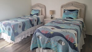 Deux lits jumeaux identiques, avec des têtes de lit et des pieds de lit assortis, chacun agrémenté d’une couvre-lit et de coussins sur le thème de la mer.