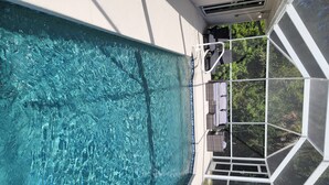 Une piscine d’un bleu éclatant, dotée d’une structure de verre aux lignes géométriques, entourée d’un mur blanc et offrant une vue sur la verdure.