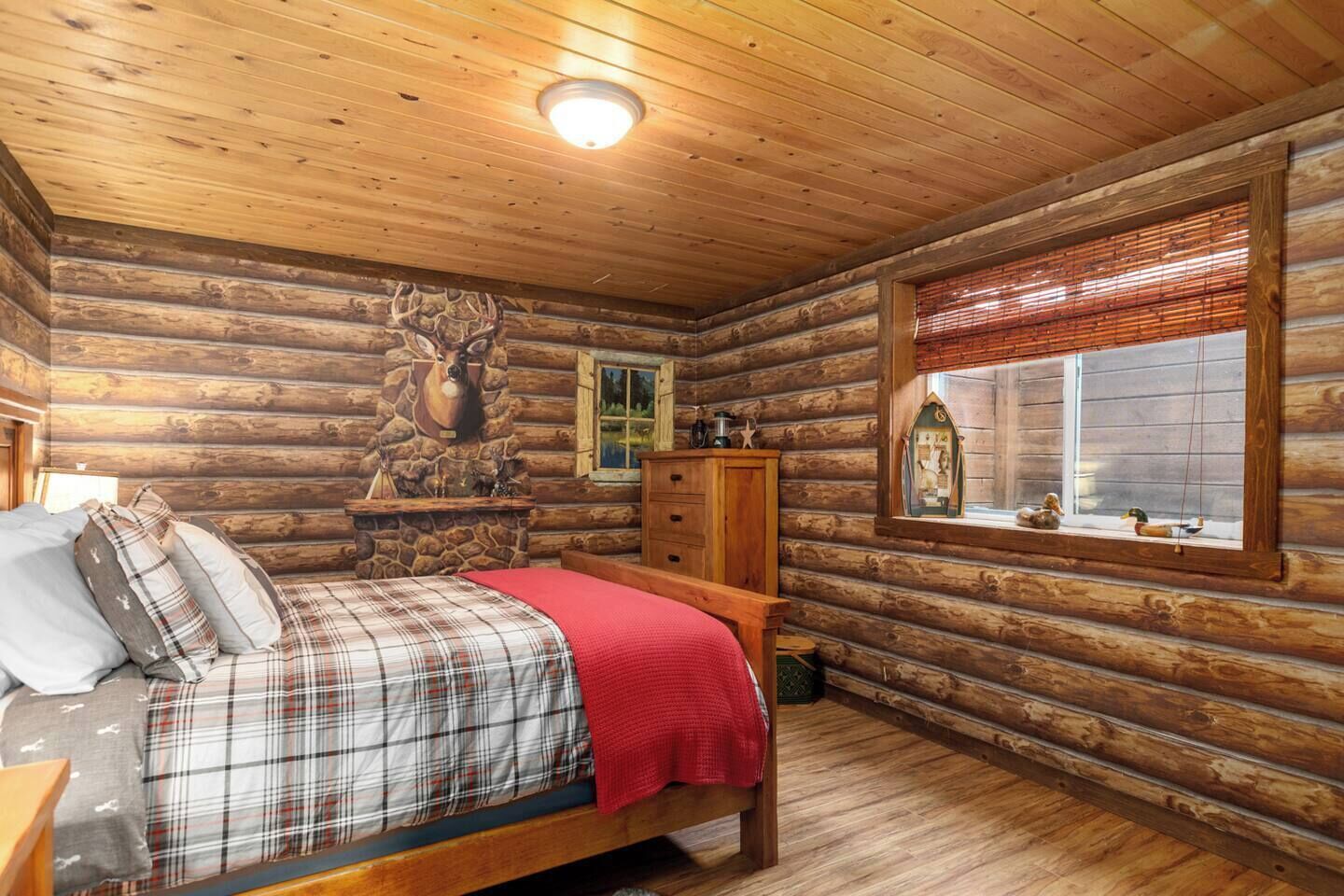 Une chambre dans un chalet en rondins, avec un lit, une commode et une tête de cerf décorative accrochée au mur.