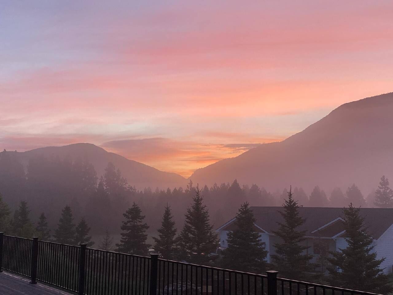 Et bjergrigt landskab med solopgang eller solnedgang, med et hus med synligt tag og et hegn i forgrunden.