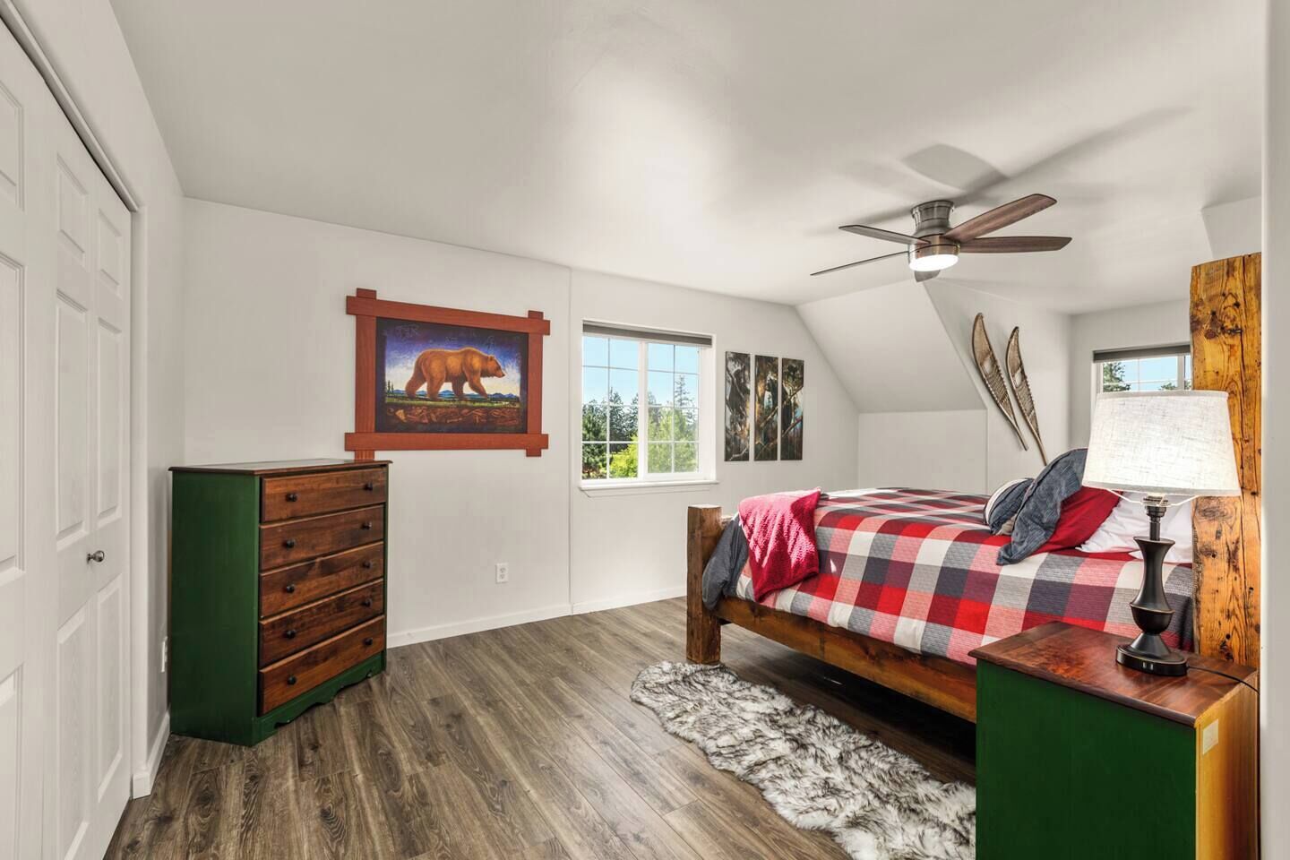 Un dormitorio con una cama de madera, un ventilador de techo, un aparador y un cuadro de un oso.