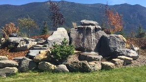 Eine natürliche Felsformation mit einem kleinen Wasserfall, umgeben von Herbstlaub und Bergen im Hintergrund.