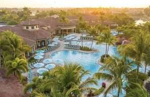 A resort with a large central pool, multiple lounge areas with umbrellas, and palm trees. -  PLAYERS CLUB AVAILABLE, Professionally Renovated, 3 Bedroom Golf Condo (Naples)
