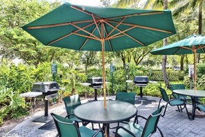 An outdoor patio with round tables and chairs, green umbrellas, and barbecue grills. -  PLAYERS CLUB AVAILABLE, Professionally Renovated, 3 Bedroom Golf Condo (Naples)