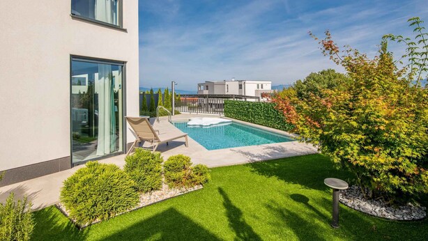 A modern building with a swimming pool, a small garden area, and a view of the surrounding landscape.