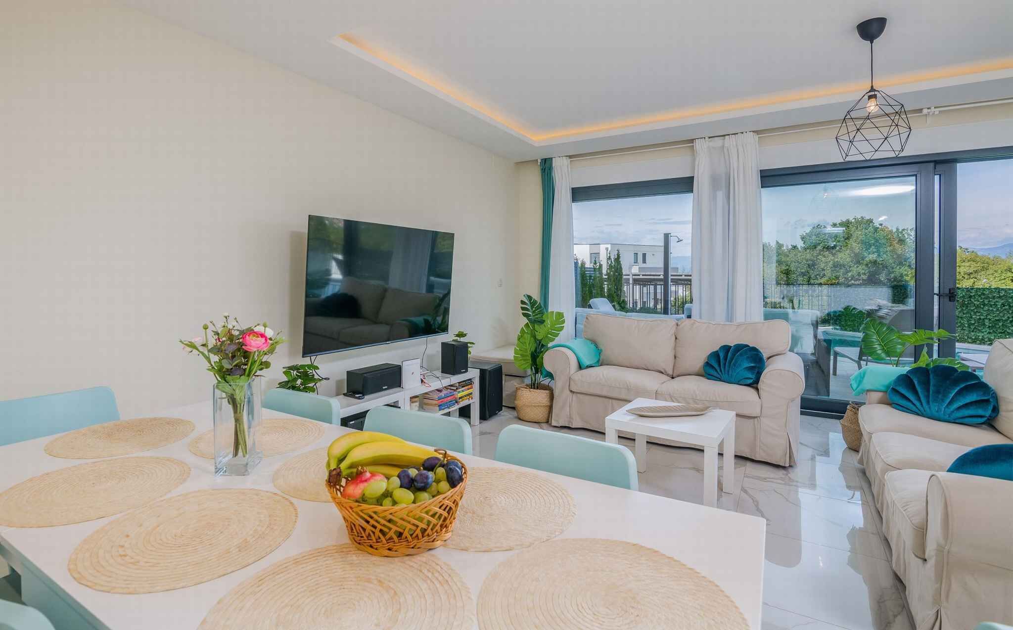 A modern living room with a flat-screen TV, comfortable seating, a dining area with placemats, and a view of the outdoors.
