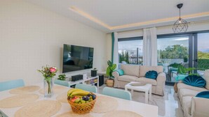 A modern living room with a flat-screen TV, comfortable seating, a dining area with placemats, and a view of the outdoors.