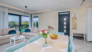 A modern living room with a sofa, coffee table, dining table, and a vase of flowers.