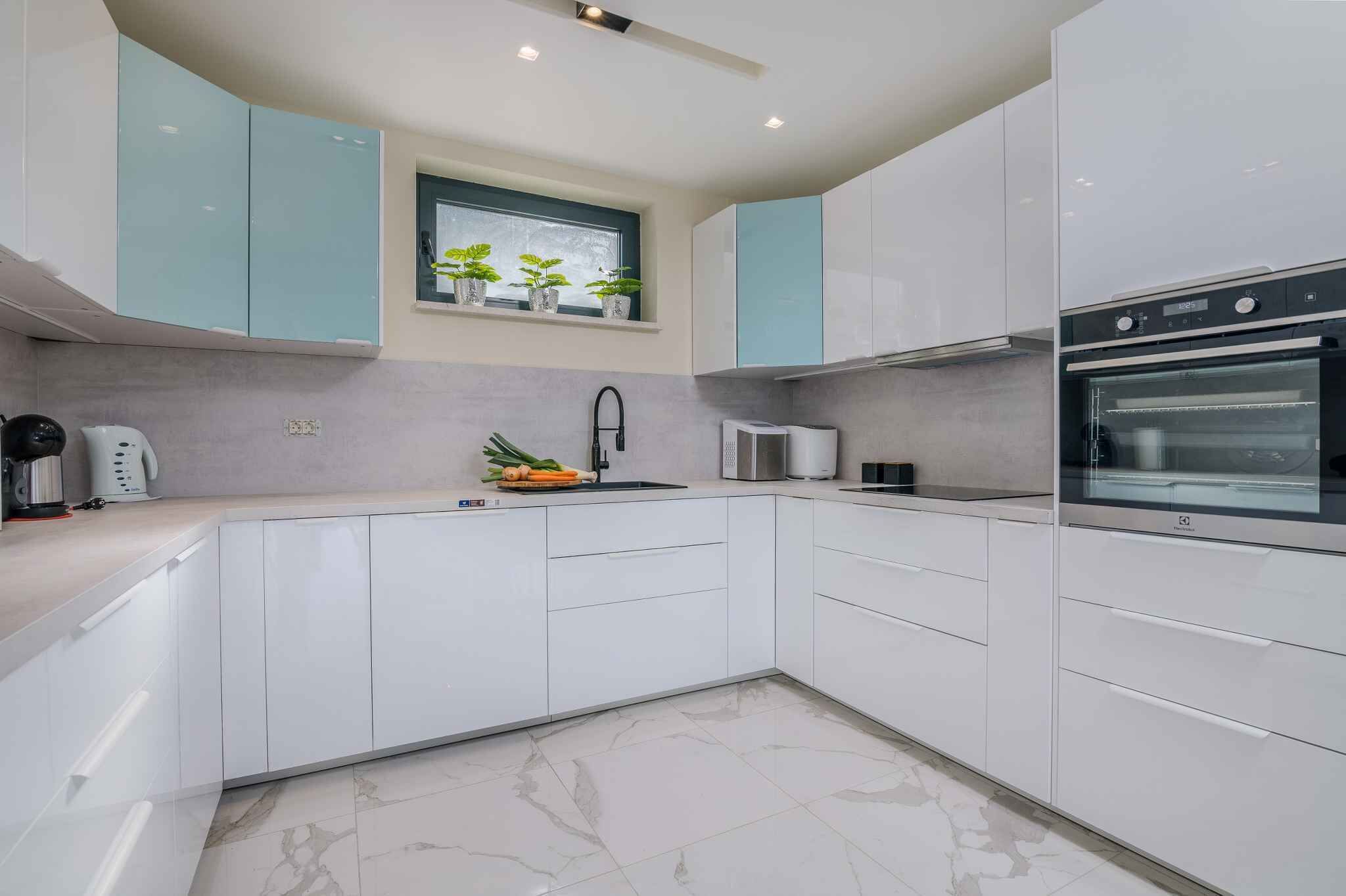 Una cocina moderna con armarios blancos, horno empotrado, microondas y una ventana con plantas.