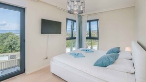 A bedroom with a large bed, a TV mounted on the wall, and a balcony with a view.