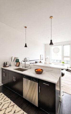 A modern kitchen with black cabinets, a white countertop, and two pendant lights.