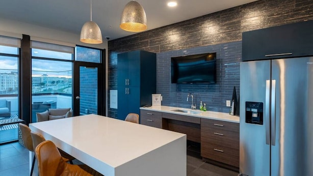 Una cocina moderna con una isla grande, muebles oscuros, electrodomésticos de acero inoxidable y vistas a la ciudad a través de amplios ventanales.