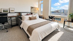 Un hotel moderno con una cama grande, un escritorio, una silla, una lámpara y vistas a la ciudad.