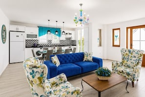 A modern living room with a blue sofa, floral armchairs, a wooden coffee table, and a kitchen in the background.