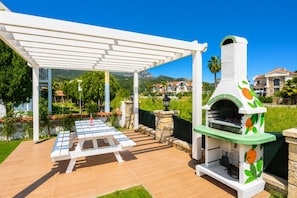 An outdoor patio with a grill, a covered seating area, and a view of a residential neighborhood.